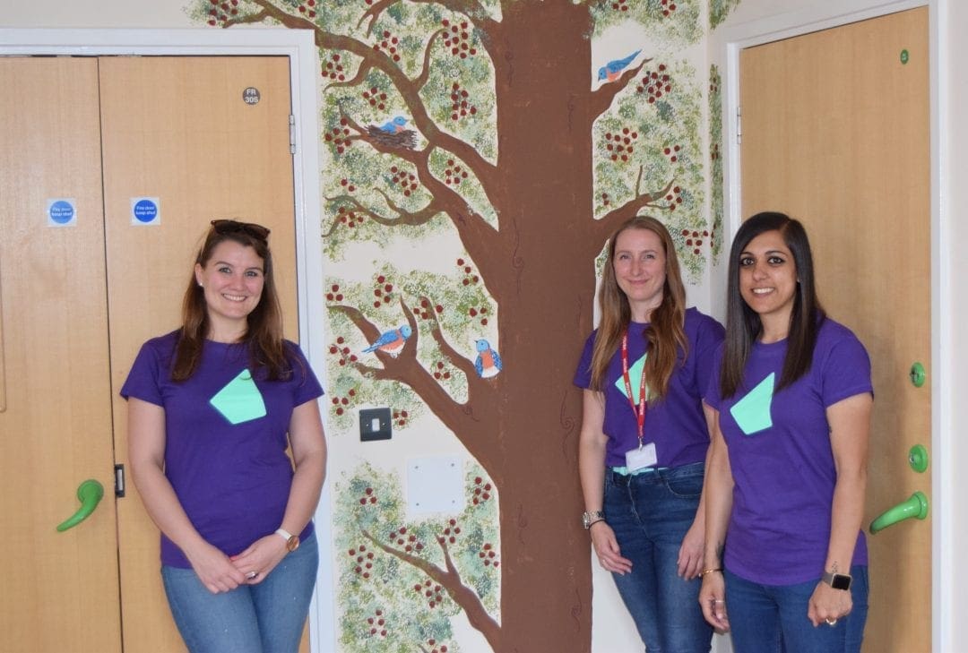 Photo of three IRESS staff members in front of the tree mural in the Willow Ward end of life room.